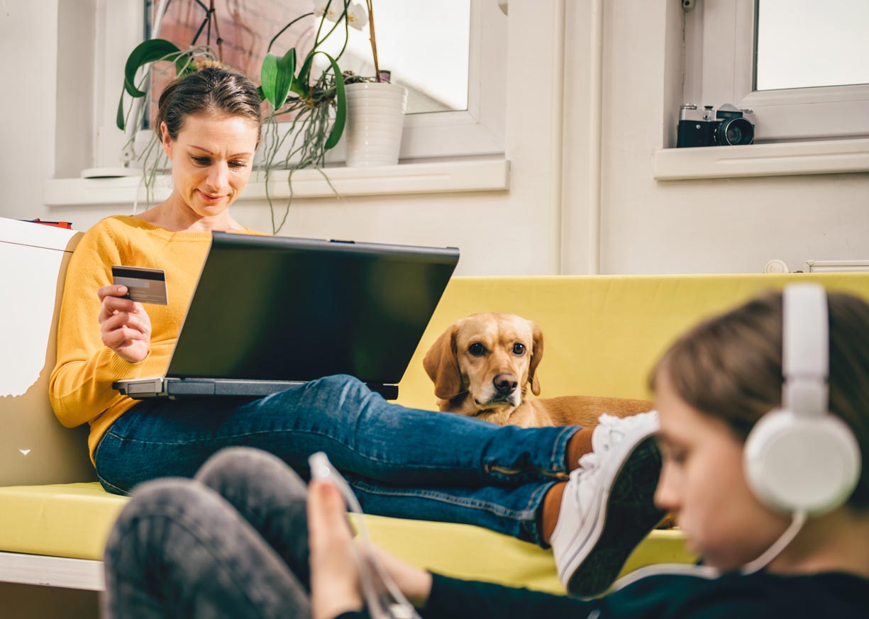 A relaxed young lady sitting with a laptop who is holding a debit card and using online banking