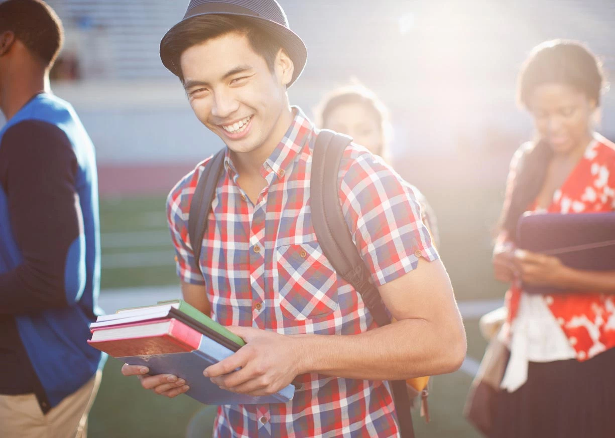 A young male student with a Student Checking account is walking with a backpack and books
