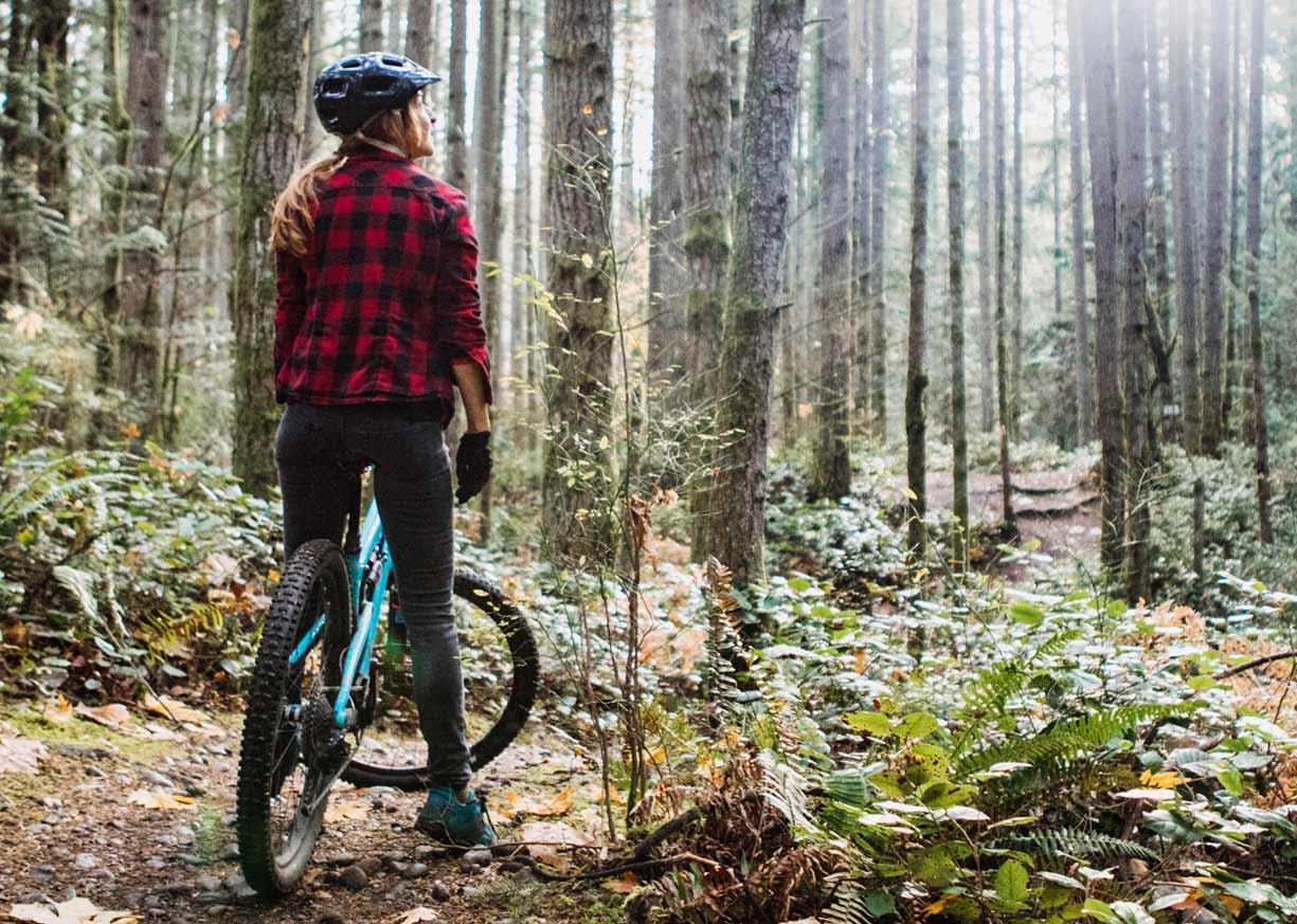 A young woman on a mountain bike who has saved money in a Money Market account is on a bike trail in the woods