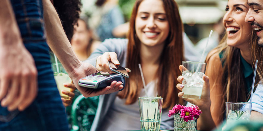 A happy group of friends in their early twenties are paying a restaurant bill with Samsung Pay on a smart phone