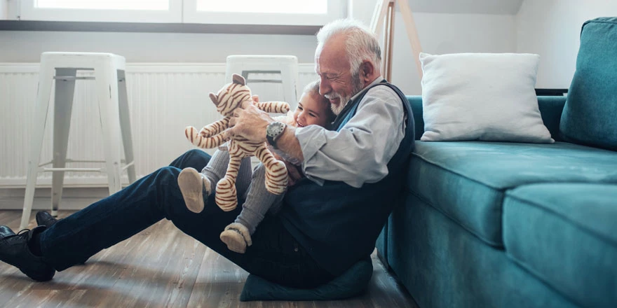 A happy grandfather who has saved for retirement with an IRA Money Market is playing with his granddaughter