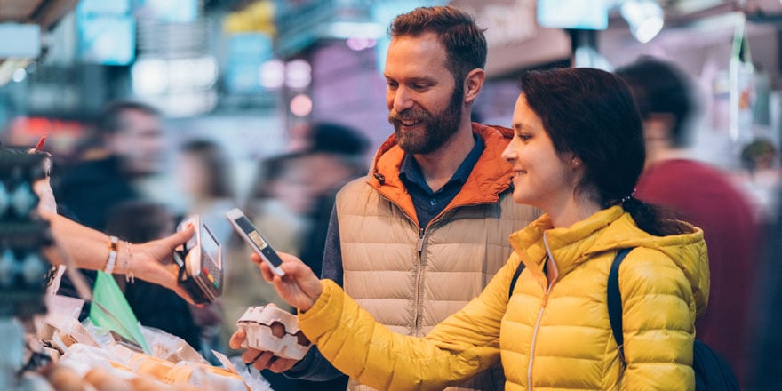 A couple smile while using a phone to make a digital payment at a grocery store with Apple Pay