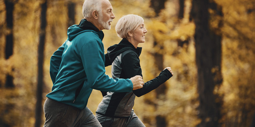 A healthy older couple who have a Health Savings Account are jogging together on a nature trail