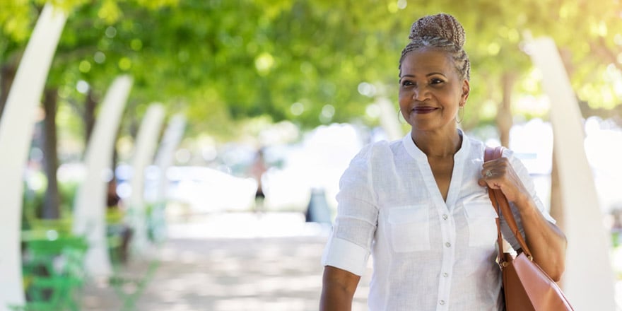 A happy woman who opened a Diamond Money Market account is smiling and walking down a path on a spring day