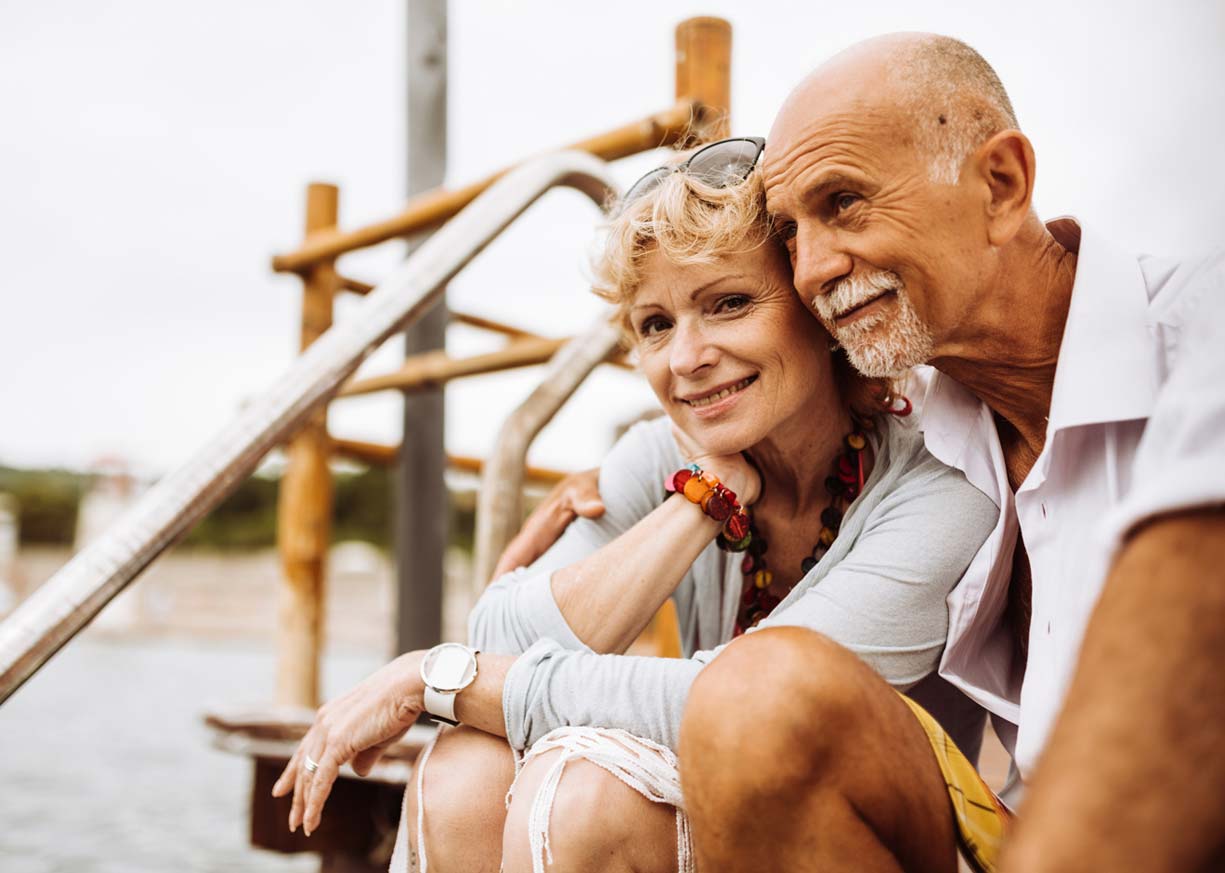 An older couple who have savings in a Diamond Money Market are happily embracing on a pier by a lake