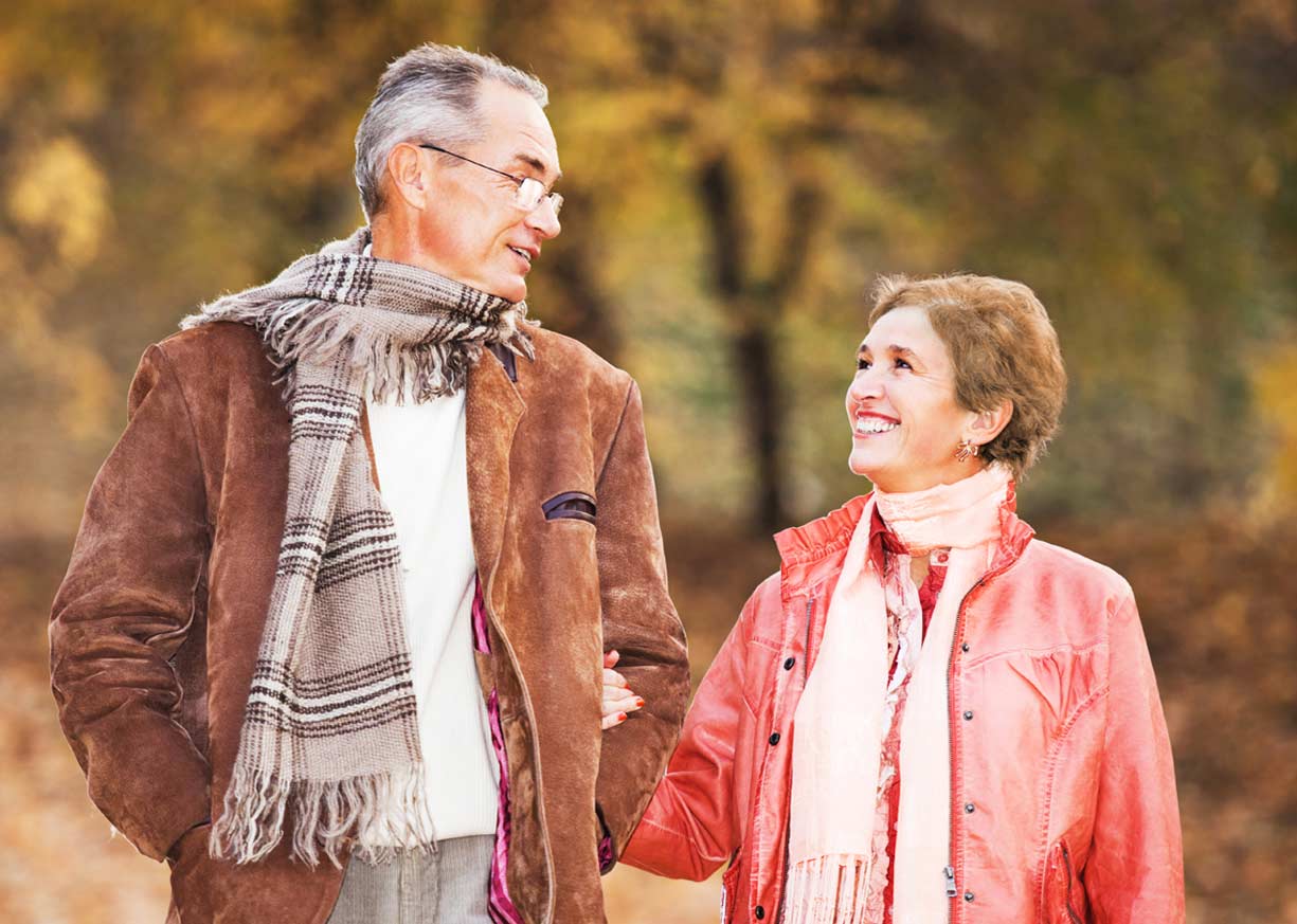 A happy middle-aged couple who are Premier Money Market Account clients are holding hands and walking in the woods