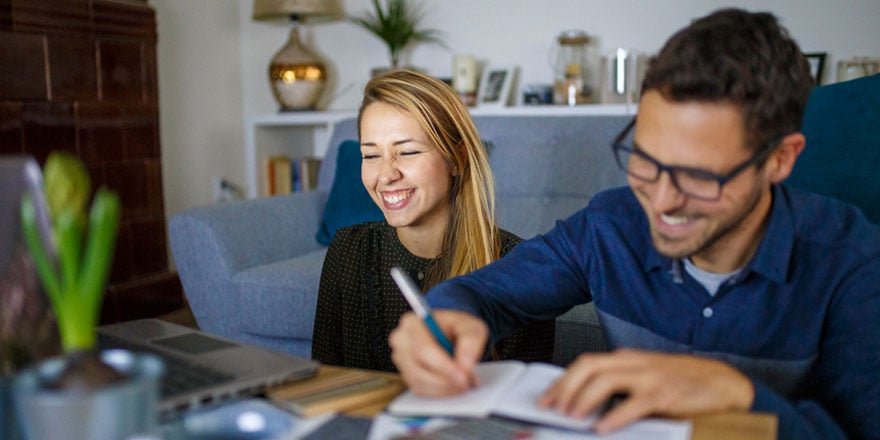 Two college-aged students are smiling and working on a laptop while discussing a Statement Savings account