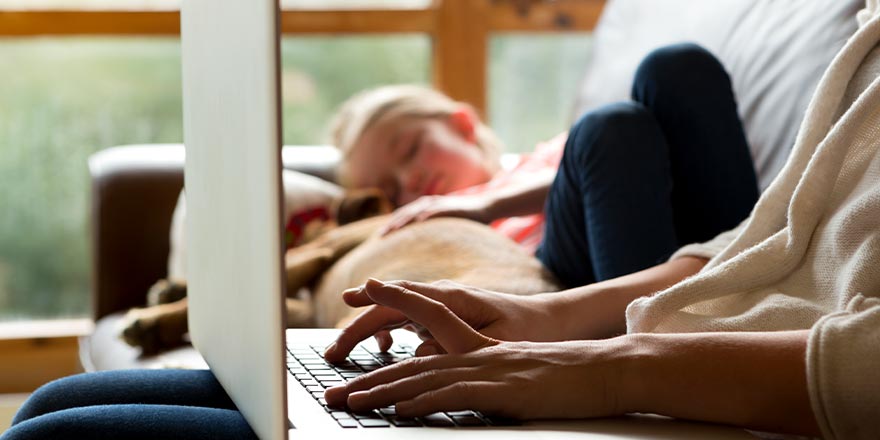 A mother makes a loan payment online while her daughter peacefully naps next to her