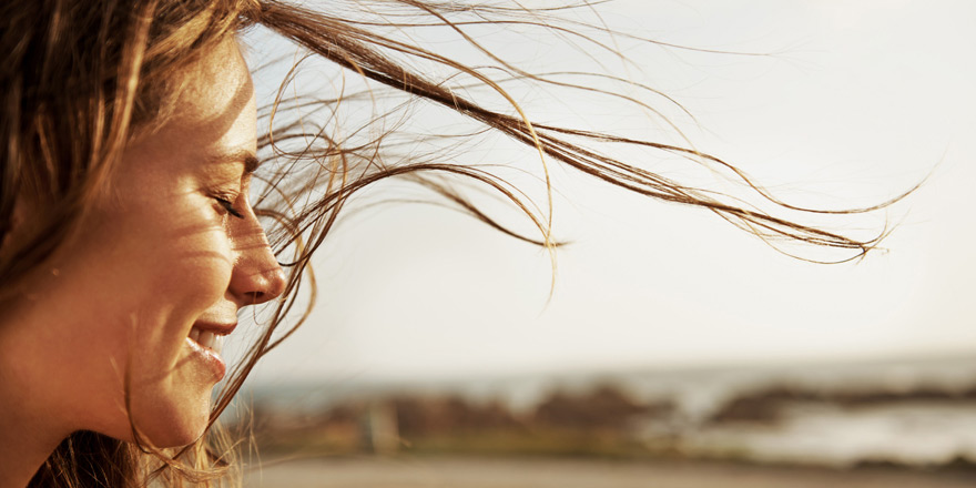 A younger woman who has overdraft protection services is smiling and enjoying a walk on the beach