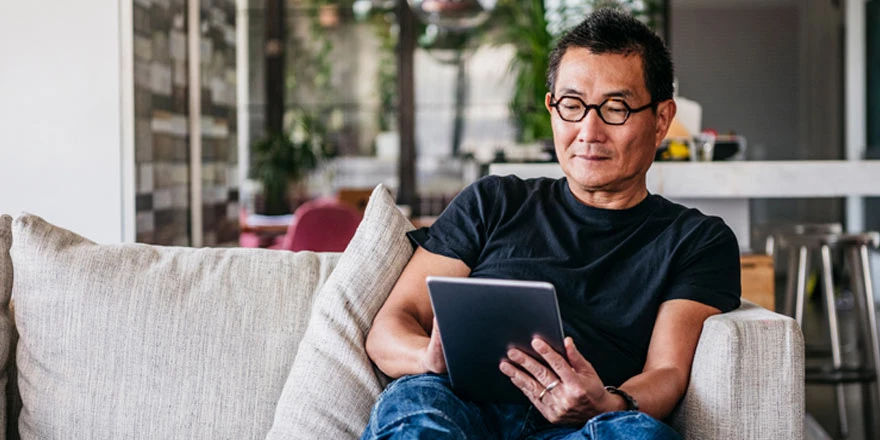 A middle-aged man on a tablet relaxes on his sofa while looking at his Investor Reserve Savings account online