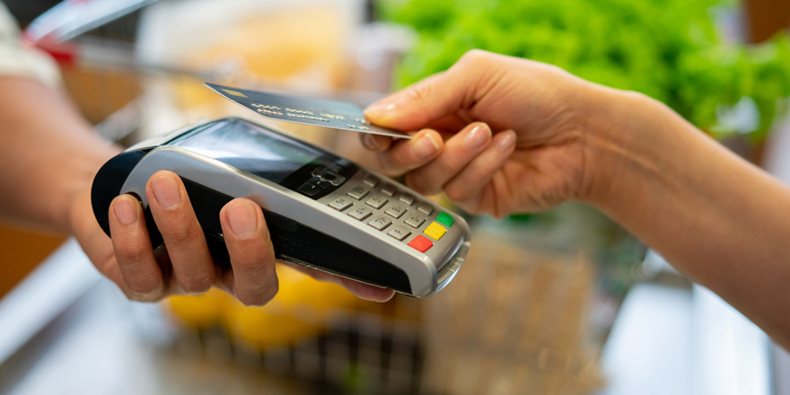 Close up of a customer handing a business owner a credit card for processing via their merchant services terminal