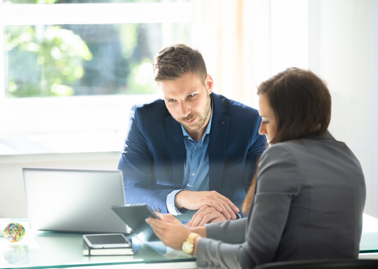 Two colleagues who are looking at a laptop and a tablet are discussing the best checking account options for their business