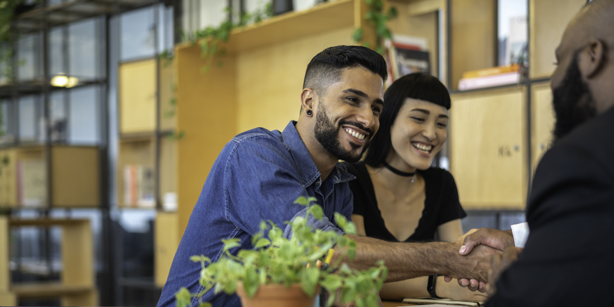 A younger couple shake hands with the owner of an alternative financial center