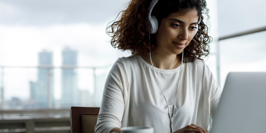 A young business owner on a laptop and using headphones is watching fraud mitigation videos