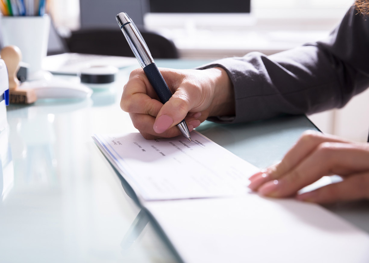 Close up of a hand writing a check to open a new business checking account