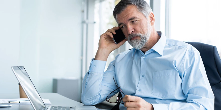 A businessman looks at a laptop while talking on his cell about liquidity management options for his business