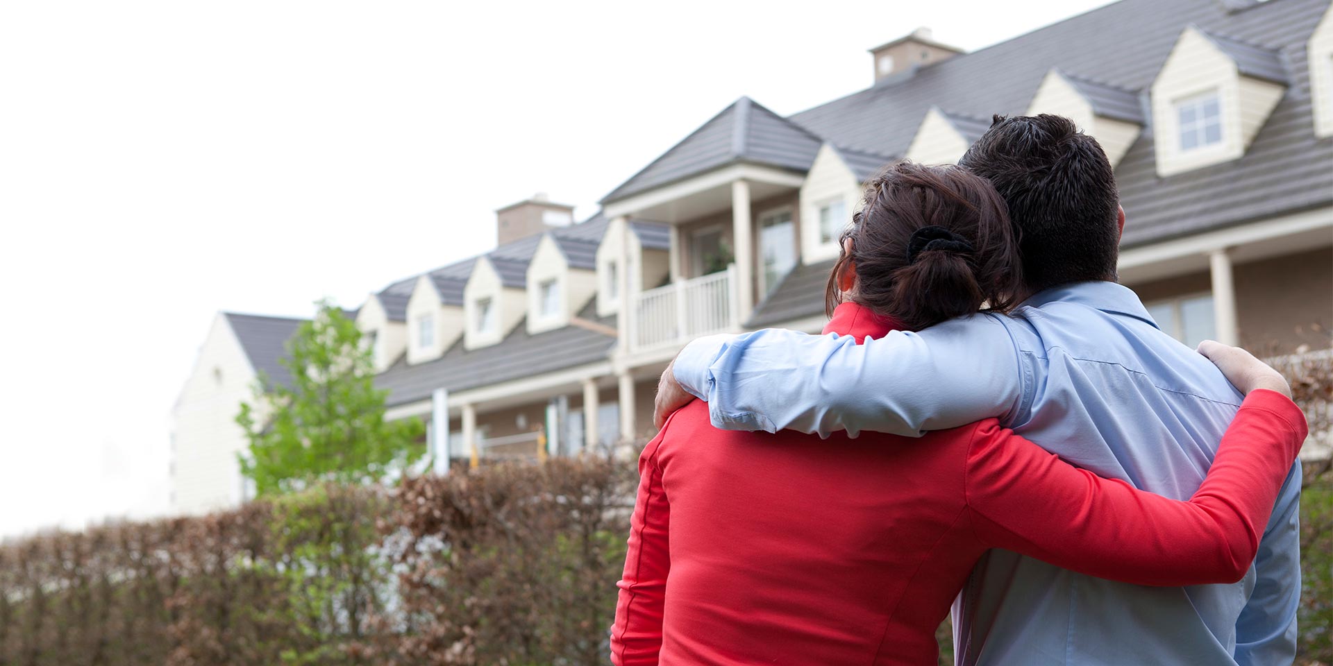 A happy couple who are private banking clients hug each other as they look at their beautiful home