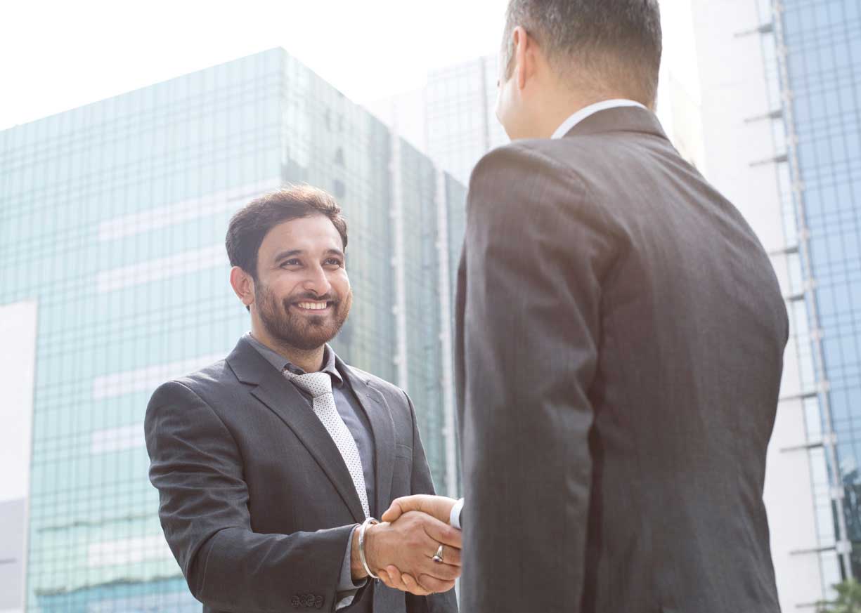 Two businessmen shake hands in front of a city skyline as they discuss Commercial Banking services