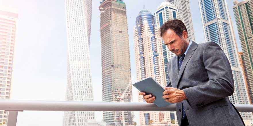 A businessman in front of a city skyline looks at his tablet to review the international banking services his business needs