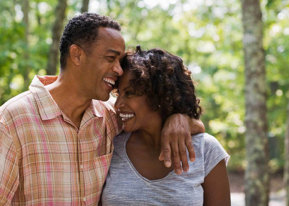 A middle-aged couple who are Investor Reserve Savings clients are hugging while walking down a forest path