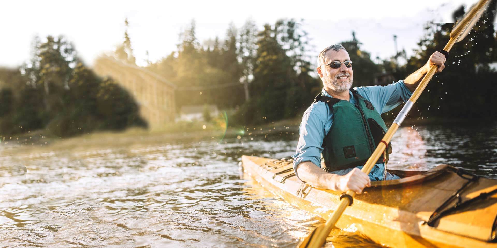 A middle aged man paddling a kayak who is a Money Market account customer