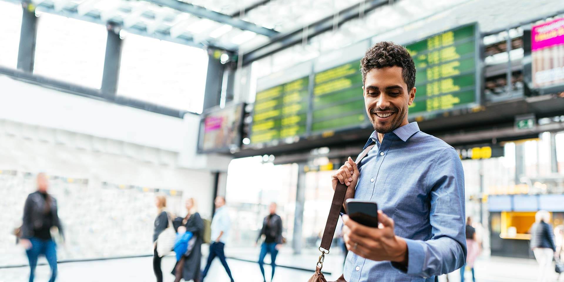 A businessman in an airport is smiling and using his phone to make a mobile deposit with the mobile banking app